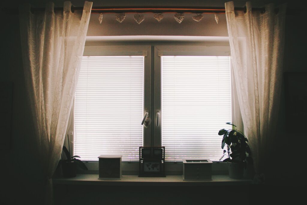 A home interior featuring a window with curtains, blinds, and potted plants.